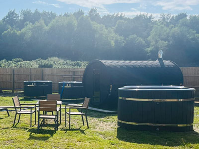 A glamping site with glamping pods, hot tubs and outdoor seating which has a view of a forest 