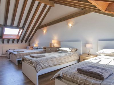 An attic room at Ebor Cottage with four beds in it and wooden ceiling beams on its sloped roof 