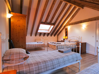 A room at Jorvik Cottage that has three beds, a sloped ceiling with wooden beams and a wardrobe 