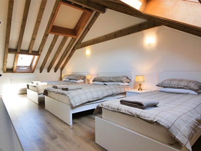 An attic room at Knavesmire Cottage with three beds, a slop ceiling and wooden ceiling beams 