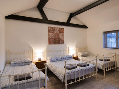 A room at Roman Cottage that has three beds sat in a row with some wall art above the beds 