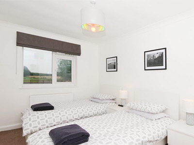 A bedroom at Pheasant Rise that has two single beds, wall art above the bed and a window with countryside views 