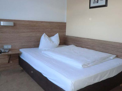 A double room with a bedside table and plain bedsheets at Hotel Andra in Munich