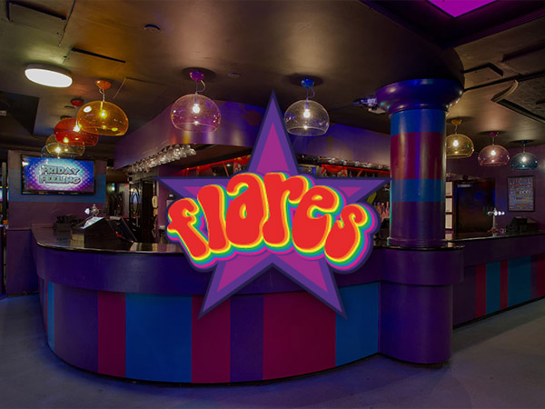 A man dressed up, pointing at Flares logo within the nightclub 