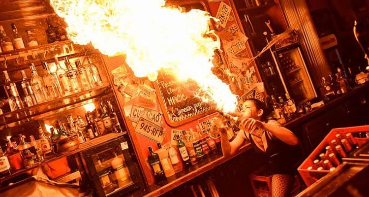 Image of a women blowing a huge flame behind a bar with alcohol