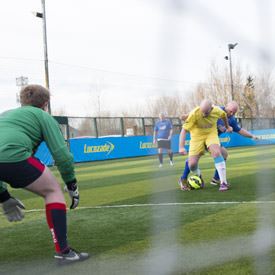 A goalkeeper in the foreground watching as two players tackle for the ball