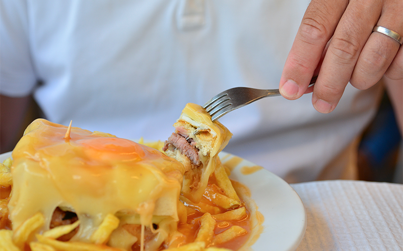 A man eating meat covered in cheese with chips 