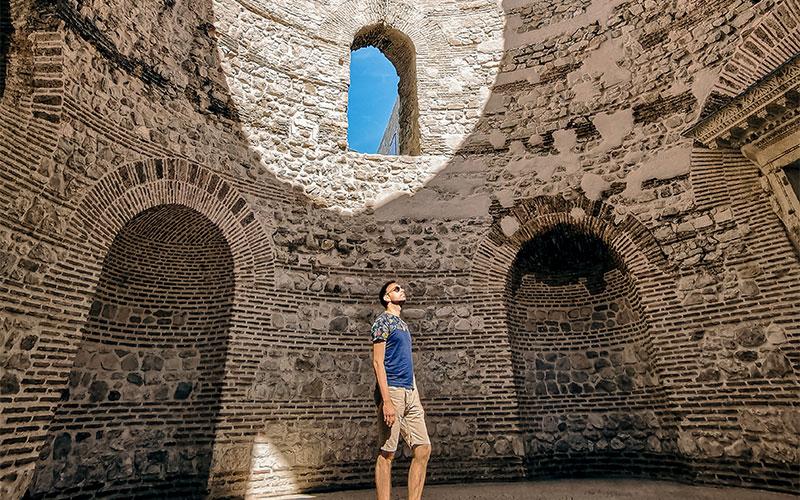 The inside of a historical looking stone building with a man looking up at the ceiling. 