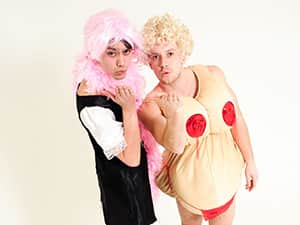 A man in a dress and pink wig, posing next to a man in a wig and a women's fatsuit