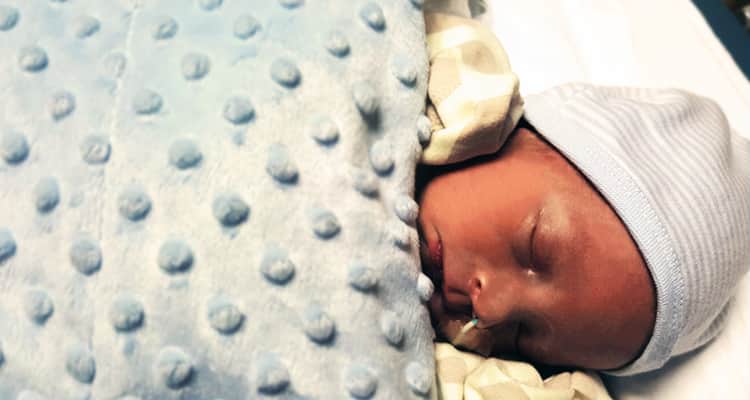 An image of a baby boy wrapped in a blue blanket at the hospital
