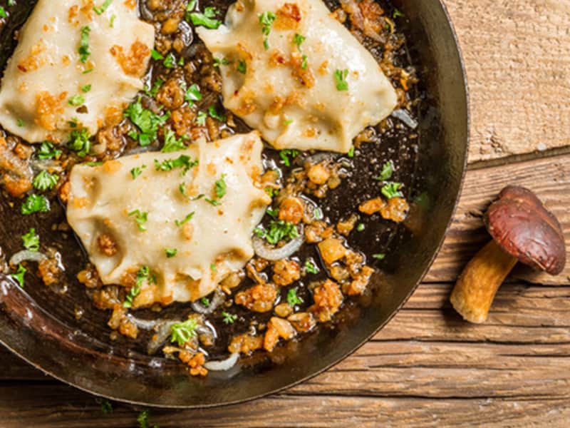 A close up of traditional dumplings in a pan, alongside a mushroom
