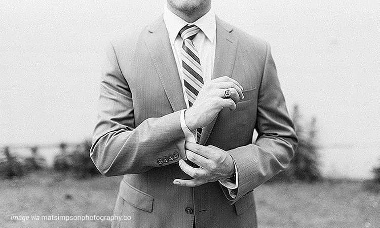 The torso of a man wearing a grey suit, adjusting his cuff