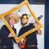 Two men posing in a photobooth with accessories whilst holding a fake photo frame