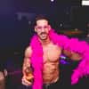 A semi-naked man posing with a pink boa around his neck 