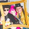 Two men and a pink gorilla posing in a photobooth with accessories, holding a fake photo frame