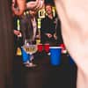 A shot through two people, showing men playing beer pong in a bar