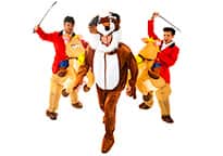 two men dressed as hunters on inflatable horseback chasing a man in a fox costume
