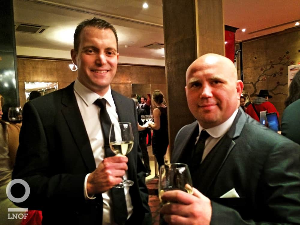 Two men in suits and holding wine glasses at a film premiere