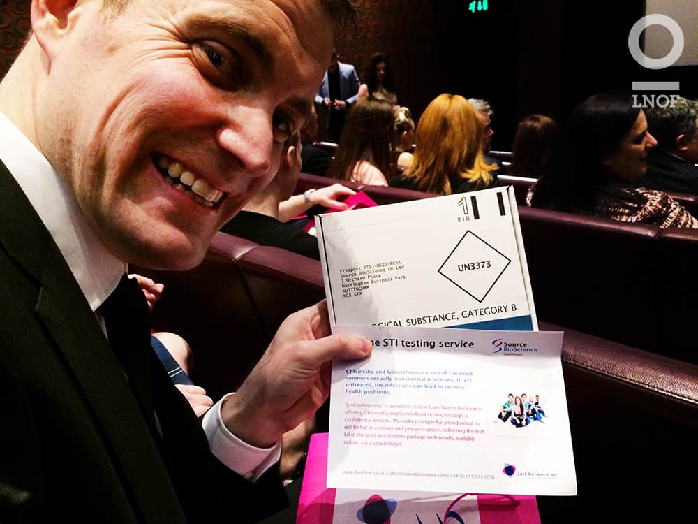 A man sat in a cinema, holding cards for a complimentary STI test
