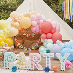 White PARTY cardboard sign with multicoloured balloons inside in front of a decorated tepee