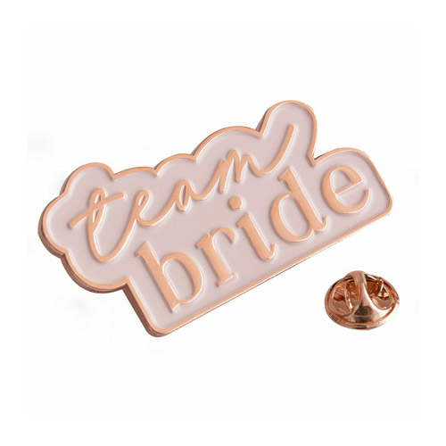 A pastel pink enamel badge with Team Bride written in rose gold on a white background.