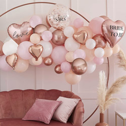 Rose gold palette hen do balloon arch in a room in front of a metal circle stand