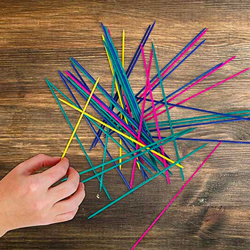 Hand picking up sticks from Pick Up Sips game on a wooden surface.