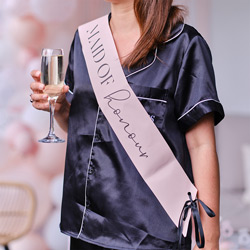 Someone wearing a maid of honour sash while holding a glass of champagne
