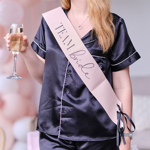 Someone wearing ateam bride sash while holding a glass of champagne