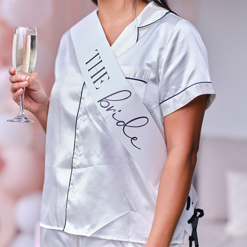 Someone wearing a bride sash while holding a glass of champagne