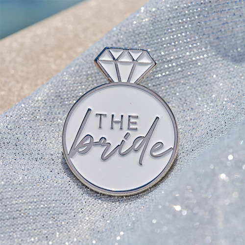 An enamel badge of a ring with the words 'the bride' in the middle 