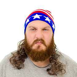 A man looking angry and wearing a stars and stripes hat with a mullet attached