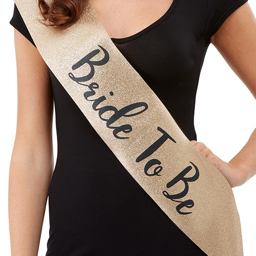 Gold glitter bride to be sash with black lettering.